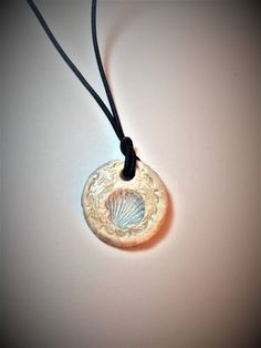 a necklace with a seashell on it is hanging from a black cord and sits on a white surface