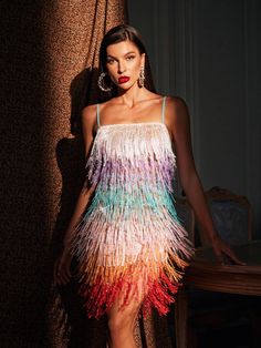 a woman standing in front of a wall wearing a dress with multicolored feathers