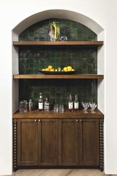 a wooden shelf filled with bottles and glasses next to a bowl of fruit on top of a counter