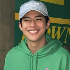 a young man wearing a green hoodie and a white hat smiles at the camera