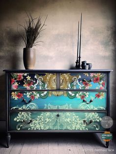 an old dresser with flowers painted on the front and sides, next to a potted plant