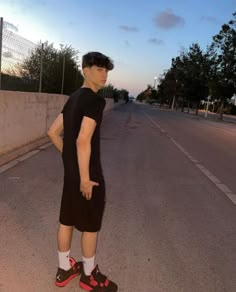 a man in black shirt and shorts standing on street with skateboard under his arm