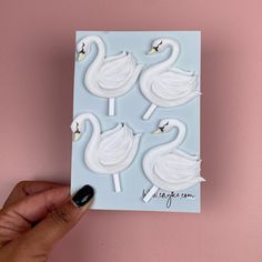 a hand holding a card with four white swans on it's sides and one black swan in the middle