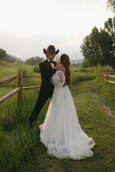 a man in a cowboy hat is hugging a woman in a wedding dress on the grass