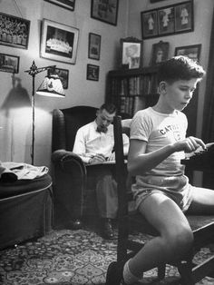 black and white photograph of boy sitting on chair looking at cell phone in living room