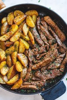 steak and potatoes in a skillet on a white tablecloth next to some bread