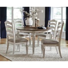 a dining room table with four chairs and a vase on top of it in front of a window