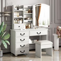 a white dressing table with mirror and stool next to a potted plant on the floor