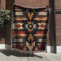 a person standing next to a brick wall holding up a blanket with an abstract design on it