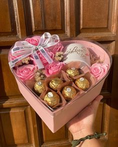 a heart shaped box with pink roses and chocolates in it is held by a hand