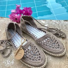 a pair of crocheted shoes next to a swimming pool with purple flowers in it