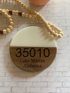 a wooden sign that says 35010 lake martin, alabama with beads and a potted plant in the background