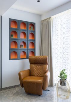 a brown recliner chair sitting in front of a wall with orange shelves on it