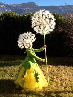 a woman in a green dress holding a large dandelion with white flowers on it