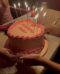 two people holding hands over a birthday cake with lit candles on it and the words happy written in pink frosting