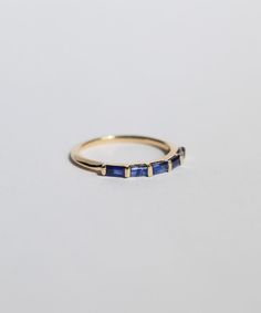 a yellow gold ring with blue sapphire stones on the sides, set against a white background