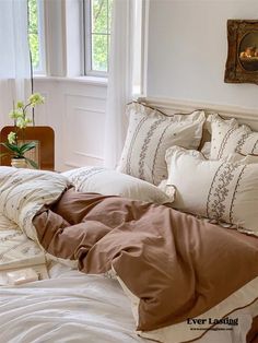 an unmade bed with white and brown comforter in a bedroom next to a window