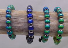 three bracelets are sitting on top of a wooden branch, one is blue and the other is green