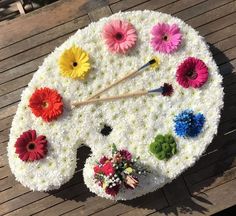 a large clock made out of flowers on a wooden table with two sticks sticking out of it