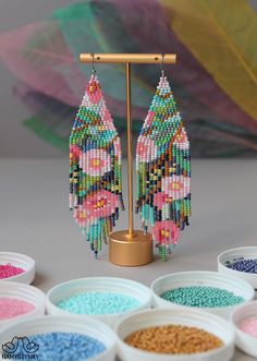 the beaded earrings are on display in front of several bowls with different colored beads