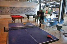 two men are playing ping pong in an indoor recreation room with tables and chairs