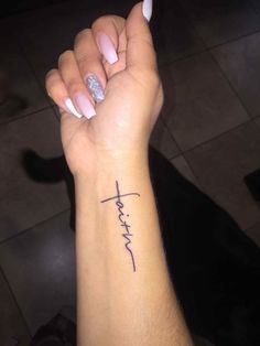 a woman's arm with a cross tattoo on it and the word faith written in cursive font