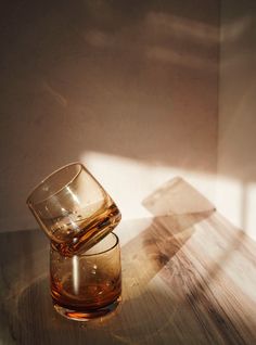 a glass sitting on top of a wooden table next to a shadow cast by the sun