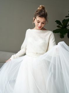 a woman in a white dress sitting on a couch wearing a long skirt and sweater