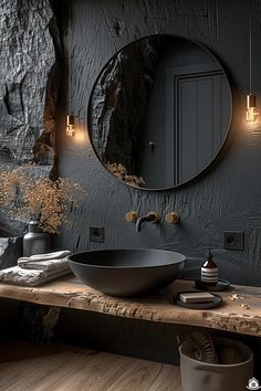 a bathroom with black walls and wood flooring, round mirror on the wall above the sink