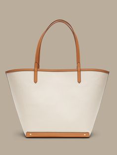 An elegant companion to everyday style, this classic tote goes anywhere with ease with spacious storage, sturdy leather trim, and a snap closure.  Sturdy leather handles.  Open top with snap closure.  Height: 16" (41cm) Width: 25" (63cm) Depth: 8" (2 Classic Top Handle Bucket Bag For Shopping, Brown Coated Canvas Bucket Bag With Leather Trim, Classic Bucket Bags With Handles, Classic Bucket Bag With Handles, Classic Top Handle Bucket Bag With Large Capacity, Classic Bucket Bag With Leather Handles, Leather Top Handle Bag With Canvas Lining, Leather Bucket Bag With Canvas Lining For Daily Use, Classic Beige Bucket Bag With Large Capacity