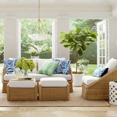 a living room with wicker furniture and large windows in the background, along with potted plants