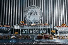 an assortment of desserts on display in front of a metal wall with the word atlassian written across it