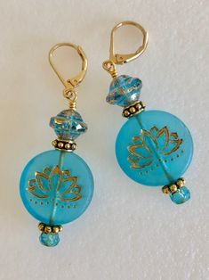 "Lovely aqua blue Czech glass lotus flower earrings with gold Picasso wash. These are large 22mm flat coin beads in a transparent matte aqua blue with same design on each side. Accented with transparent Czech glass saucer beads with mottled gold finish. All Premium Czech glass beads. Additional accents include ornate Antique gold pewter spacers and small aqua Czech rondelles. Earrings are on gold plated lever backs and are 2\" long." Blue Round Flower Earrings Hypoallergenic, Blue Round Hypoallergenic Flower Earrings, Hypoallergenic Blue Flower Earrings, Handmade Blue Round Flower Earrings, Blue Round Flower Earrings With Ear Wire, Blue Spiritual Earrings For Gifts, Adjustable Light Blue Round Earrings, Turquoise Czech Glass Flower Earrings For Gift, Blue Round Glass Earrings