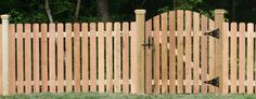 a wooden fence with an iron gate in the center and green grass on the other side