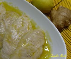 a white plate topped with sliced chicken next to a lemon and ginger on top of a yellow mat