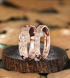 two rose gold wedding rings sitting on top of a piece of wood with leaves around them