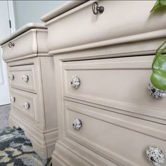 a white dresser with drawers and knobs on the bottom, next to a green plant