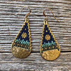 two pairs of gold and blue beaded earrings sitting on top of a wooden table