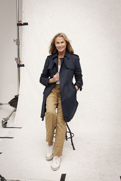 a woman sitting on a chair in front of a white backdrop wearing a trench coat