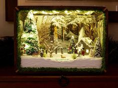 a lighted christmas scene is displayed in a frame on top of a table with other decorations