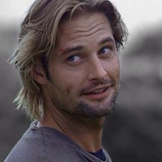 a man with blonde hair and blue eyes looks up at the camera while wearing a gray shirt