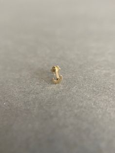 a small gold earring sitting on top of a gray surface with no one around it