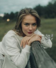 a woman leaning on a fence with her hand on the rail and looking at the camera