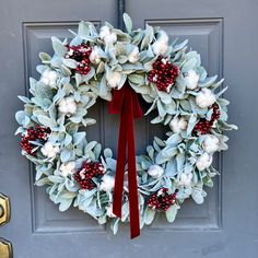 a wreath with white flowers and red berries hangs on the front door's gray door