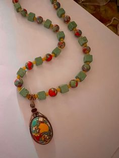 This pendant necklace consists of a stunning and unusual mosaic stone with accent of garnet. There are alternating stones in necklace of turquoise cubes and round mosaic stones with  spectacular colors!! With a magnet clasp, this is an easy choice to grab and go because it goes with a myriad of looks and outfits. It is super comfortable snd priced to sell Green Rectangular Beaded Necklace Gift, Multicolor Turquoise Necklace With Faceted Beads, Rectangular Green Beaded Necklace For Gift, Bohemian Multicolor Turquoise Necklace With Faceted Beads, Green Turquoise Necklace With Colorful Beads As A Gift, Turquoise Necklace With Oval Gemstone Beads For Gift, Turquoise Necklace With Oval Gemstone Beads As A Gift, Unique Faceted Beads Gems And Cabochons For Gifts, Polished Oval Beads Turquoise Necklace For Gift