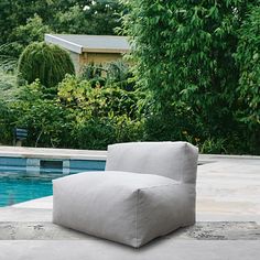 an outdoor lounge chair next to a swimming pool with trees and bushes in the background