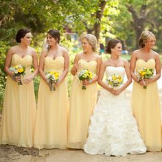 a group of women standing next to each other wearing yellow bridesmaid dresses and holding bouquets