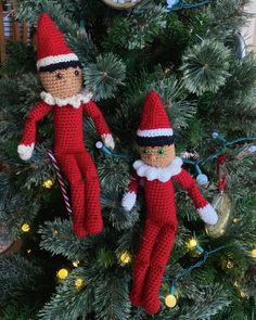 two crocheted elfs hanging from a christmas tree in front of a clock