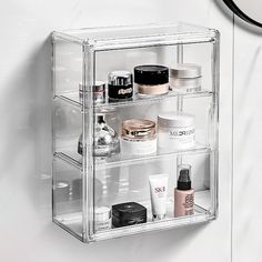 an acrylic display case holds cosmetics and other beauty products in front of a wall clock