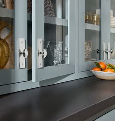 a bowl of oranges sitting on top of a kitchen counter next to cabinets with glass doors